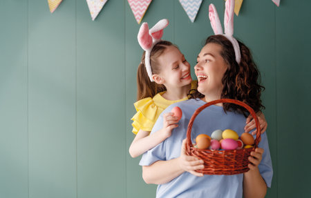 Cute little child wearing bunny ears on Easter day. Girl and mother with painted eggs.の写真素材