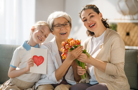 Happy mother's day! Child daughter is congratulating mom and grandma giving them flowers tulips. Granny, mom and girl smiling on light grey background. Family holiday and togethernesの写真素材