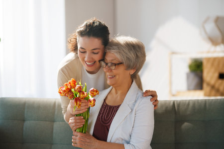 Beautiful young woman and her mother with flowers tulips in hands at home.の写真素材