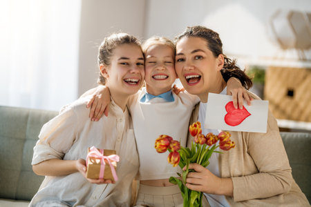 Happy mother's day. Children daughters congratulating mom and giving her flowers and postcard. Mum and girls smiling and hugging. Family holiday and togetherness.の写真素材