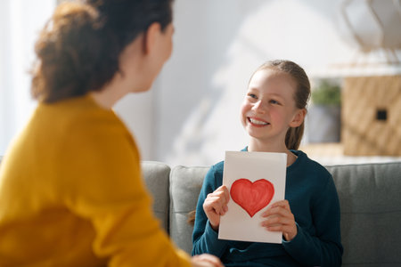 Happy mother's day. Child daughter is congratulating mom and giving her postcard. Mum and girl smiling and hugging. Family holiday and togetherness.の写真素材