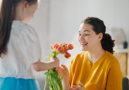 Happy mother's day. Child daughter is congratulating mom and giving her flowers. Mum and girl smiling. Family holiday and togetherness.の写真素材