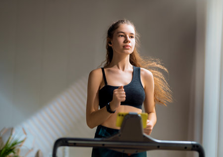 Home workout. Young woman running on a treadmill indoors.の写真素材