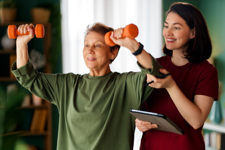 Senior woman doing dumbbell exercise. A nurse helping with physical therapy at homeの写真素材