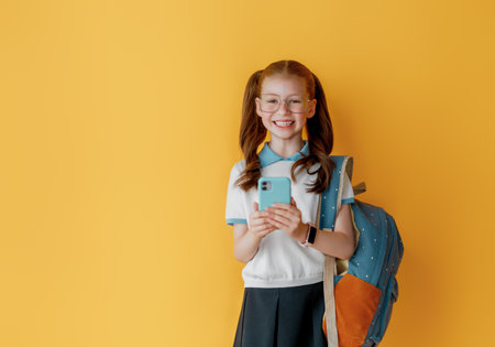 Cute happy teenager standing on bright yellow background. Child with backpack, girl is ready to back to school.の写真素材