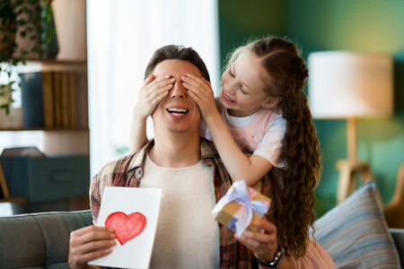 Child daughter is congratulating her father and giving him postcard. Dad and girl are smiling and hugging. Family holiday and togetherness.の写真素材