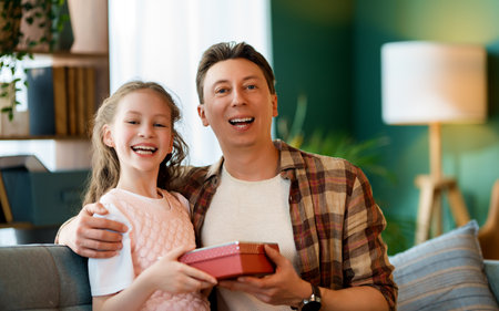 Child daughter is congratulating her father and giving him a gift. Dad and girl are smiling. Family holiday and togetherness.の写真素材