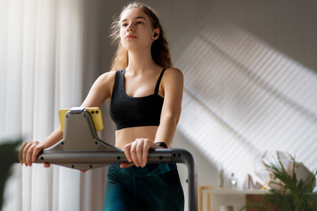 Home workout. Young woman running on a treadmill indoors.の写真素材