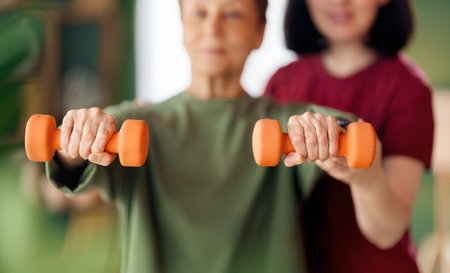 Senior woman doing dumbbell exercise. A nurse helping with physical therapy at homeの写真素材