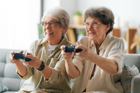 Two senior women friends or sisters playing console video game at home.の写真素材
