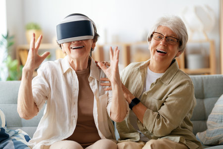 Two senior women playing console games wearing vr goggles at home.の写真素材
