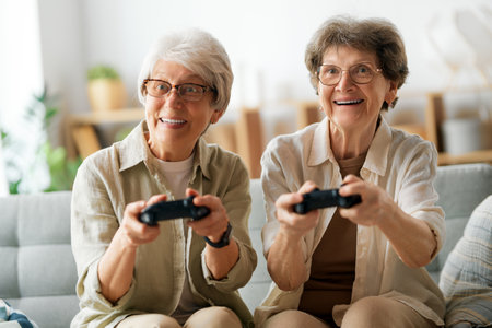 Two senior women friends or sisters playing console video game at home.の写真素材