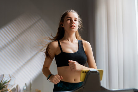Home workout. Young woman running on a treadmill indoors.