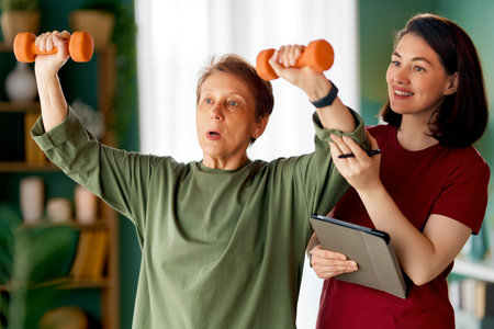 Senior woman doing dumbbell exercise. A nurse helping with physical therapy at homeの写真素材