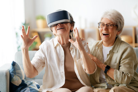 Two senior women playing console games wearing vr goggles at home.の写真素材