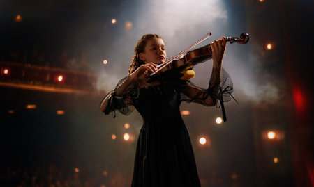 Young girl in black dress playing violin on stageの写真素材