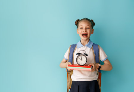 Cute happy teenager standing on bright light blue background. Child with backpack, girl is ready to back to school.の写真素材