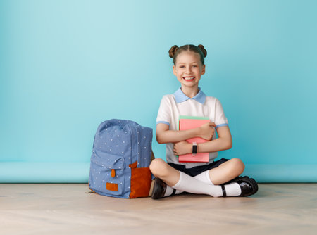 Cute happy teenager standing on bright light blue background. Child with backpack, girl is ready to back to school.の写真素材