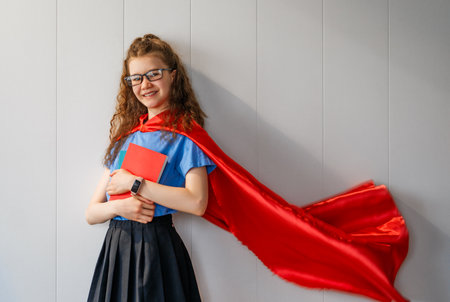 A superhero student. A schoolgirl with books against a wall.の写真素材