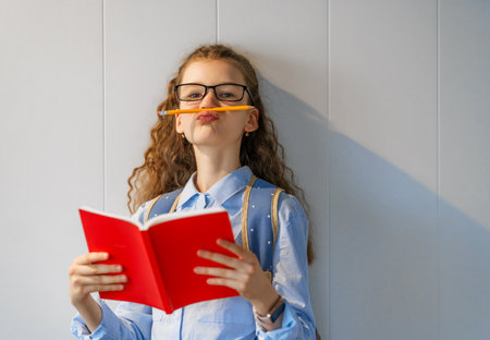 Cute happy teenager standing on grey wall background. Child with book, girl is ready to back to school.の写真素材