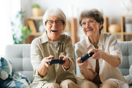 Two senior women friends or sisters playing console video game at home.の写真素材