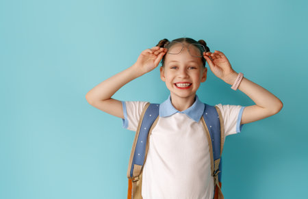 Cute happy teenager standing on bright light blue background. Child with backpack, girl is ready to...