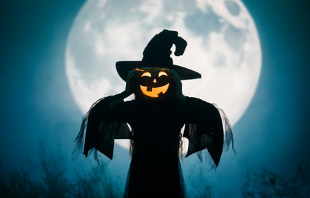 Girl dressed in witch costumes for Halloween. Kid standing on full moon background.の写真素材