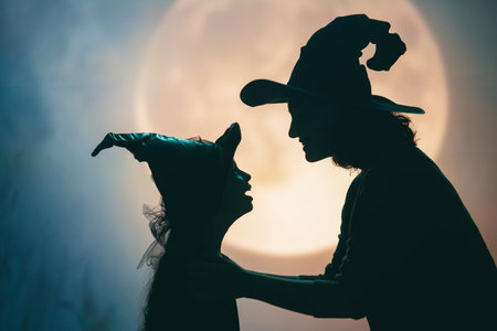 Woman and her daughter dressed in witch costumes for Halloween. Family standing on full moon background.の写真素材