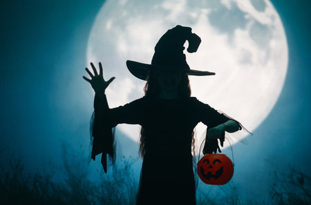 Girl dressed in witch costumes for Halloween. Kid standing on full moon background.の写真素材
