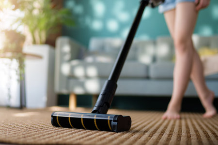 Close up of a young woman vacuuming floor with wireless vacuum cleaner in the living room. Household and useful technology concept.の写真素材