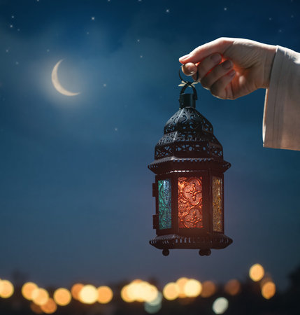 Ornamental Arabic lantern with burning candle glowing at night mosque background. Festive greeting...