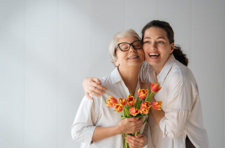 Beautiful young woman and her mother with flowers tulips in hands on white wall background.の写真素材