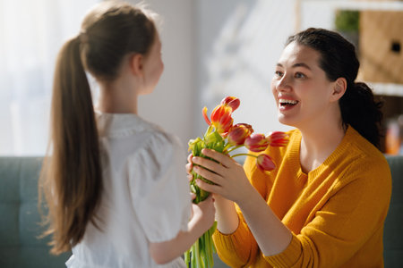 Happy mother's day. Child daughter is congratulating mom and giving her flowers. Mum and girl smiling. Family holiday and togetherness.の写真素材