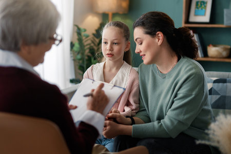 Emotional and supportive family therapy session featuring a mother and daughter engaging with a compassionate therapist. The cozy home environment and gentle interaction evoke trust, empathy, connection, and the importance of mental health support, making this image ideal for illustrating family counseling, healthcare, and emotional wellbeing.の写真素材