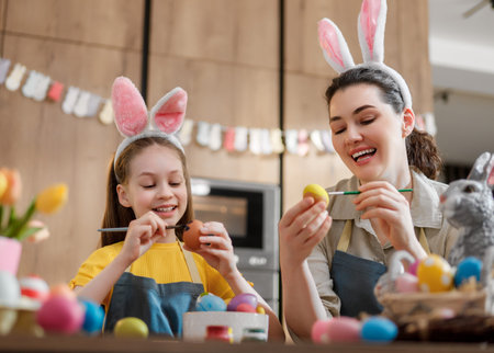 Joyful mother and daughter duo wearing bunny ears, painting colorful Easter eggs. Capturing family...