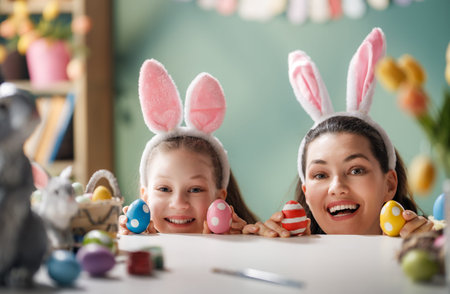 Joyful mother and daughter wearing pink bunny ears headbands, smiling and holding vibrant Easter...
