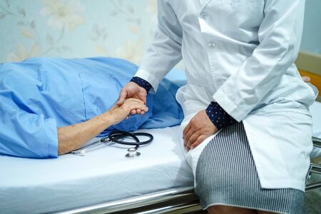 Asian nurse physiotherapist doctor care, help and support senior or elderly old lady woman patient lie down in bed at hospital ward : healthy strong medical concept.の写真素材