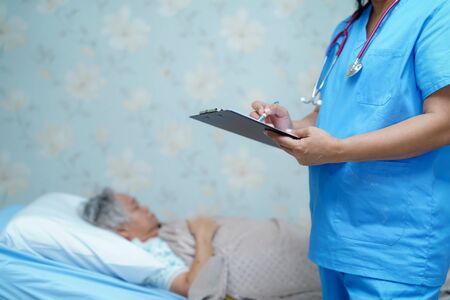 Doctor writing down the diagnosis on clipboard while Asian senior or elderly old lady woman  lying on bed in nursing hospital ward : healthy strong medical concept.の写真素材