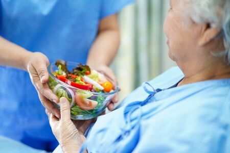 Asian senior or elderly old lady woman patient eating breakfast healthy food with hope and happy while sitting and hungry on bed in hospital.の写真素材