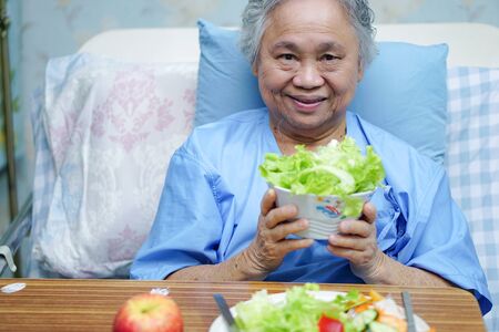 Asian senior or elderly old lady woman patient eating breakfast healthy food with hope and happy while sitting and hungry on bed in hospital.の写真素材