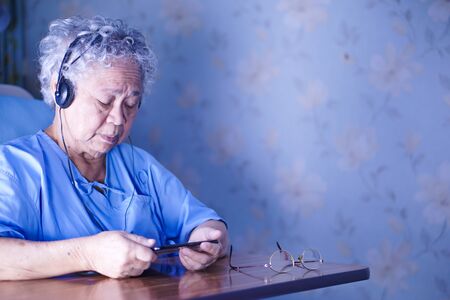 Asian senior or elderly old lady woman patient use earphone while lie down and happy on bed in nursing hospital ward : healthy strong medical conceptの写真素材