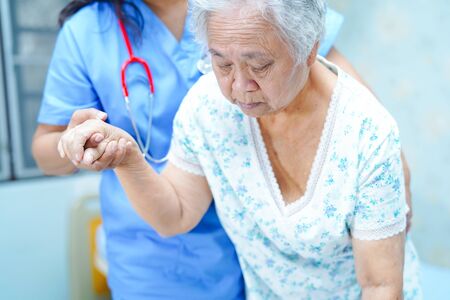 Asian nurse physiotherapist doctor care, help and support senior or elderly old lady woman patient lie down in bed at hospital ward : healthy strong medical concept.の写真素材