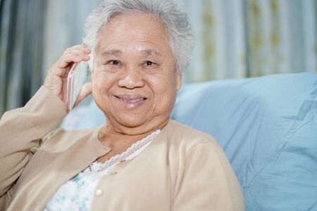 Asian senior or elderly old lady woman patient with credit card talking on the mobile phone while sitting and happy on bed in nursing hospital ward : healthy strong medical conceptの写真素材