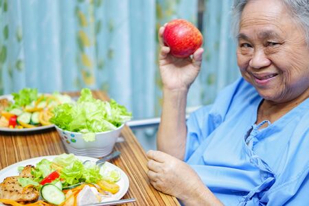 Asian senior or elderly old lady woman patient eating breakfast healthy food with hope and happy while sitting and hungry on bed in hospital.の写真素材