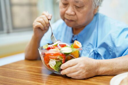 Asian senior or elderly old lady woman patient eating breakfast healthy food with hope and happy while sitting and hungry on bed in hospital.の写真素材