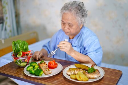 Asian senior or elderly old lady woman patient eating breakfast healthy food with hope and happy while sitting and hungry on bed in hospital.の写真素材