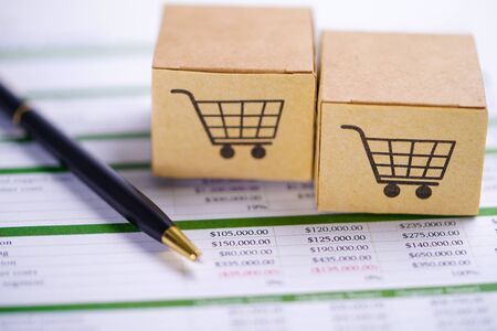 Box with shopping cart logo on spreadsheet paper and pen.