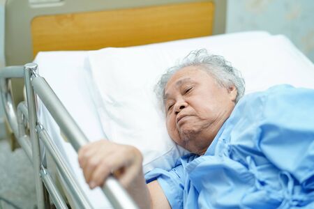 Asian senior or elderly old woman patient lie down handle the rail bed with hope on a bed in the hospital.の写真素材