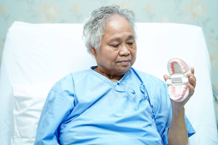 Asian senior or elderly old woman patient holding to use denture on the bed in nursing hospital ward...