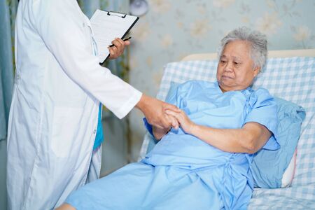 Doctor talking about diagnosis and note on clipboard with Asian senior or elderly old lady woman while lying on bed in nursing hospital ward : healthy strong medical concept.の写真素材